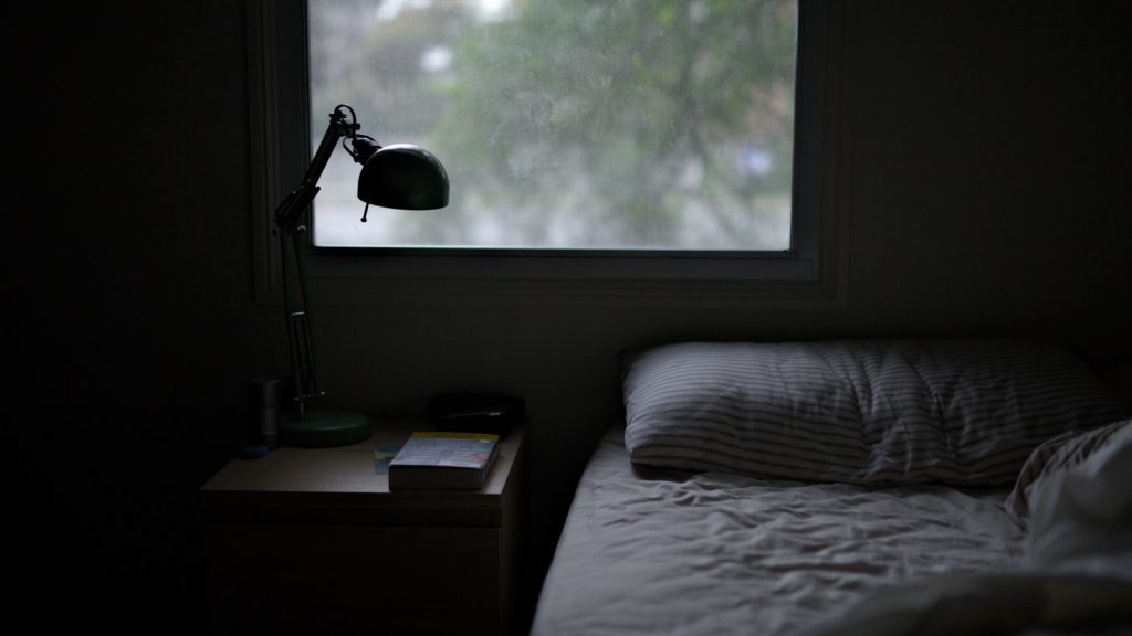 Chambre à coucher dans la pénombre, verre d'eau posé sur la table de nuit