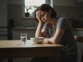 Femme fatiguée attablée devant un verre d'eau et un bol de bouillon au petit matin